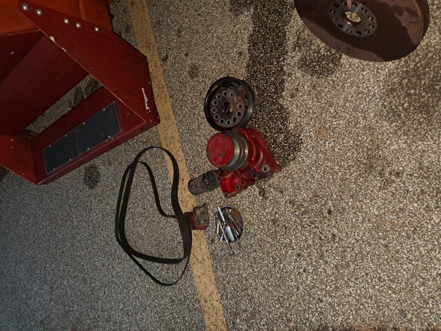 Removed engine pulleys, serpentine belt, and brackets laid out on the ground during disassembly