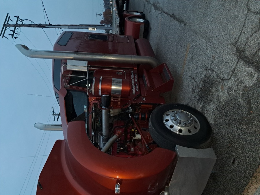 Red semi truck with hood open showing the full engine bay during inspection