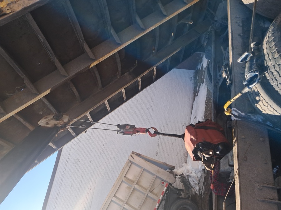 Under a heavy dump truck performing repairs with rigging and chain equipment